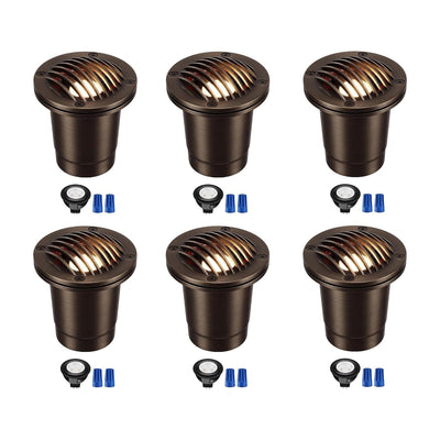 Set of 6 black low voltage in-ground well lights installed in a garden bed, illuminating warm white light upward at plants and foliage at night